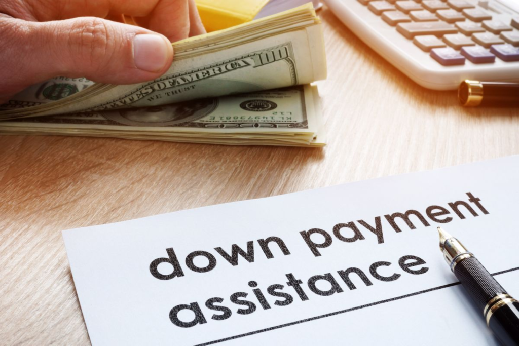 A hand holding cash next to a document labeled "down payment assistance" with a pen and calculator.
