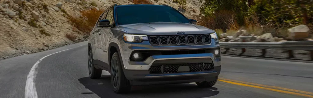 Front view of a Jeep Compass in motion, showcasing a compact SUV on a scenic highway.
