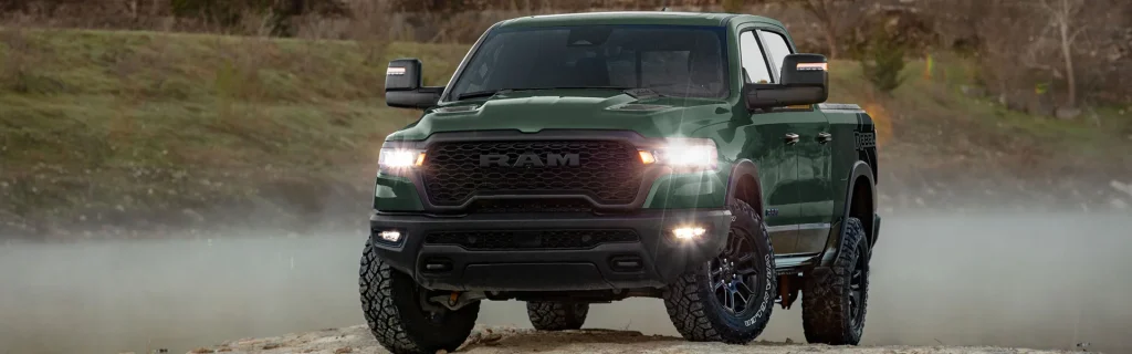 Green Ram 1500 pickup truck driving off-road on a rugged trail with dust kicking up.
